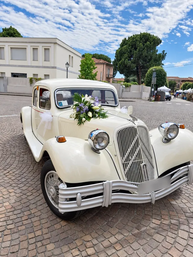 Auto d’epoca bianco crema con fiori lilla e bianchi in una piazza