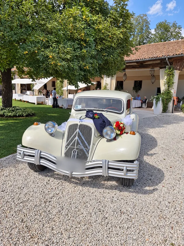 Auto d’epoca bianco crema con rose e nastro blu nel giardino di una villa