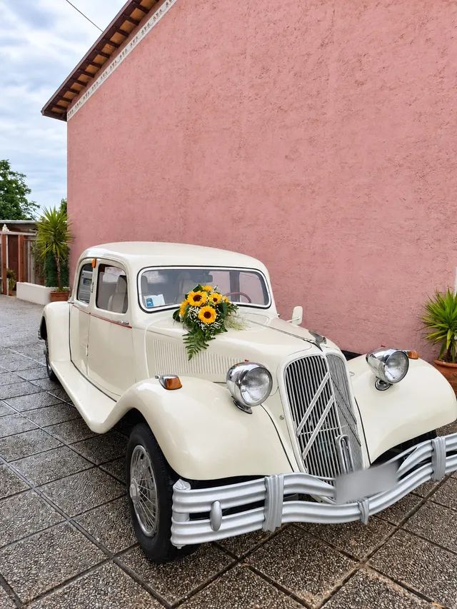 Auto d’epoca bianco crema con girasoli davanti a un muro rosa
